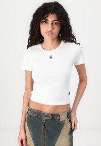 T-shirt di cotone bianco con maniche corte e scollatura rotonda; presenta un piccolo logo nero sul petto; design aderente.