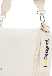 Borsa bianca testurizzata con un design a pattern, dotata di una chiusura in metallo argentato e di un'etichetta che recita "I ❤️ Desigual." Sono visibili anche la tracolla regolabile.