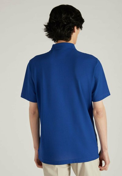 Camisa polo azul con collar y mangas cortas, hecha de tela suave. Presenta un dobladillo recto y aberturas en los lados para mayor facilidad de movimiento.