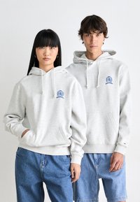 Gray hoodies with kangaroo pockets, drawstrings, and blue embroidered logo. Casual fit; worn by two models with denim bottoms.