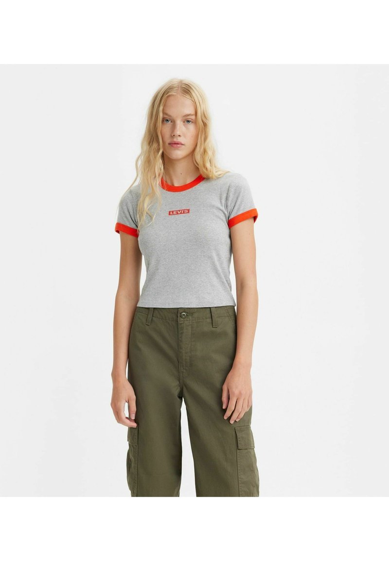 Camiseta de algodón gris con cuello y mangas cortas rojas; presenta un logo central rojo de Levi's. Combinada con pantalones cargo de color verde oliva.