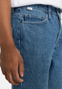 Lichtblauwe denim jeans hebben een klassiek vijfzakkenontwerp, een metalen knoopsluiting en een klein label aan de tailleband.