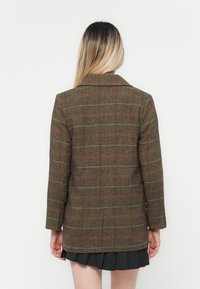 Braun kariertes Blazer im Fischgrätenmuster mit strukturiertem Design, das rot-weiße Karomuster zeigt. Das Blazer verfügt über einen einzigen Schlitze und eine glatte Textur.