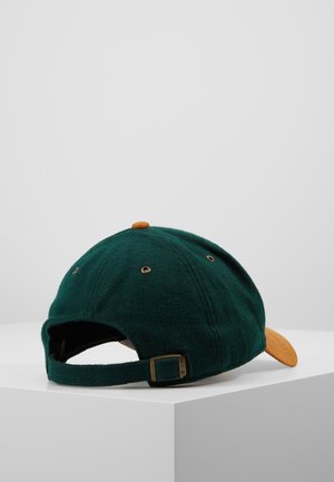 Casquette de baseball en laine vert foncé avec sangle réglable et boucle en laiton, présentant une visière incurvée en daim couleur beige et un bouton sur le dessus.