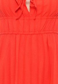 Rode, gestructureerde jurk met een keyhole-halslijn en een geraffineerde taille. Verticale strepen creëren een subtiel patroon in de stof. Zachte, vloeiende materialen.