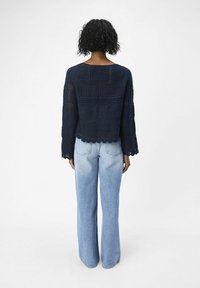 Top de punto de ganchillo azul marino con mangas largas, dobladillo festonado y patrón de calado, combinado con jeans de pierna ancha azul claro.