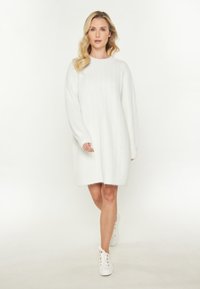 Paksu valkoinen cable-knit-neulemekko, jossa on pyöreä kaula-aukko ja pitkät hihat, rento malli ja ribattu helma, yhdistetty valkoisiin tennareihin.