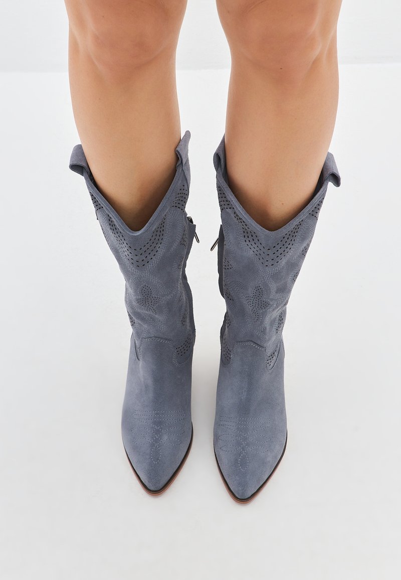 Botine gri din suede, cu vârful ascuțit, detalii decorative perforate și un design cu manșetă pliată. Închidere cu fermoar pe o parte.