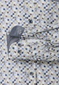 Heren overhemd met lange mouwen en knoopsluiting, voorzien van een geometrisch patroon in blauw, grijs en beige; de manchetten zijn omgeslagen, waardoor de donkere binnenstof zichtbaar is.