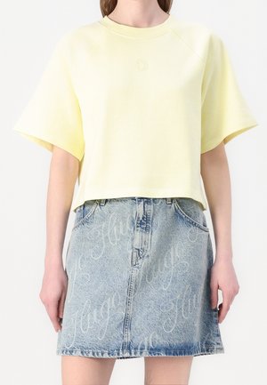 Żółta krótka bluza z krótkimi rękawami raglanowymi, zestawiona z jasnoniebieską spódnicą dżinsową z powtarzającym się wzorem logo.