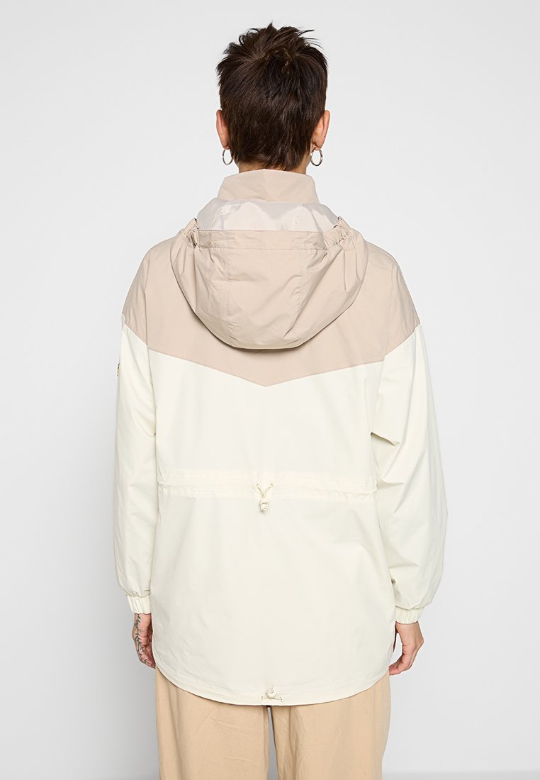 Giacca leggera bianca con una parte superiore beige. Presenta un cappuccio, polsini elasticizzati e un cordoncino in vita per una vestibilità regolabile.