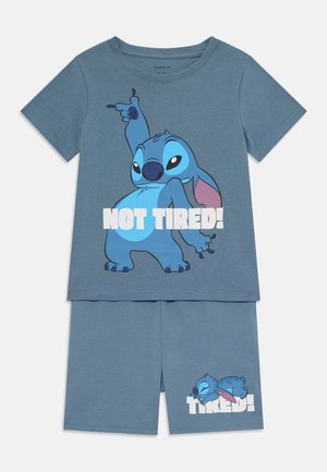 Blauwe katoenen korte pyjama's met een cartoonfiguur met roze accenten. Het shirt toont "NIET MOE!" en de shorts tonen het figuur dat slaapt.