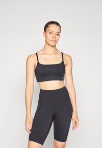 Bralette atlético negro con tirantes finos y escote cuadrado, combinado con pantalones cortos de ciclismo negros de cintura alta que cuentan con bolsillos laterales y una textura suave.