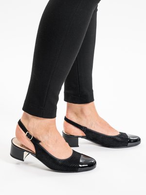 Personne portant des chaussures à talons bas blocs avec bride arrière noires, en tissu texturé et bouts lisses, associées à un pantalon noir ajusté.