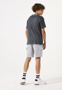 Maglietta grigia a maniche corte con vestibilità rilassata, abbinata a pantaloni cargo grigi chiari e sneakers bianche con dettagli neri.