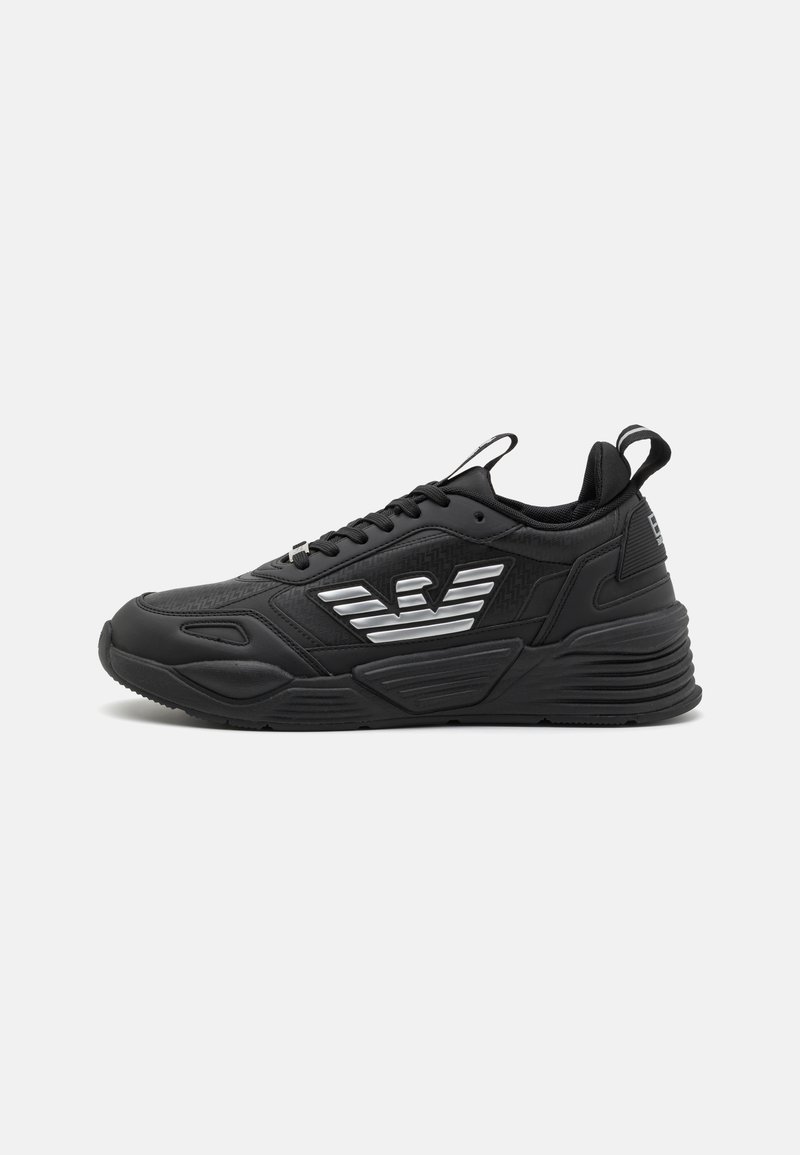 Baskets de sport noires en matériau synthétique, avec des accents texturés et un logo en argent distinct sur le côté. Elles présentent une semelle texturée et des lacets.