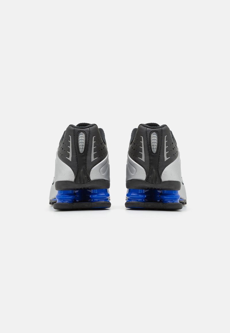Baskets de sport noires et grises avec une surface texturée, dotées d'un amorti bleu au niveau du talon et de trous de ventilation sur les côtés.