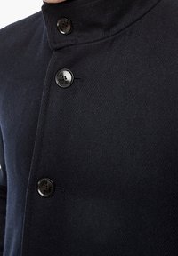 Navy wool-blend coat with a high collar, featuring two large black buttons and a herringbone texture, displaying subtle stitching details.