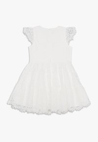 Vit spetsklänning med korta, volangärmar, en figurnära bodice och en utsvängd kjol med en scalloped nederkant. Detalj av stängning på baksidan synlig.