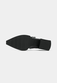 Chaussure en cuir noir avec une semelle en caoutchouc texturée, dotée d'un talon bloc et d'une fermeture éclair latérale pour un enfilage facile.