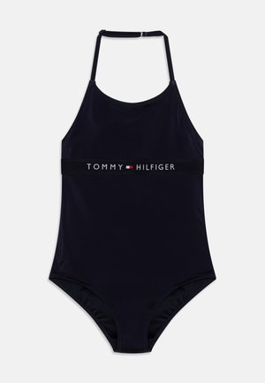 Mørkeblå heldraktbadebukse med tynne stropper og et logo-bånd med "TOMMY HILFIGER" i hvitt og rødt. Glatt, elastisk stoff.