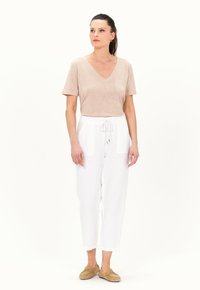 T-shirt beige a collo v- con maniche corte, abbinato a pantaloni in lino bianchi larghi con due tasche frontali e vita con cordoncino elastico.
