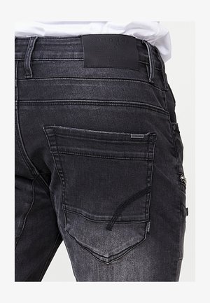 A fekete farmernadrág sima dizájnnal rendelkezik, strukturált felülettel. Hátsó zsebekkel és logózott bőr címkével a deréknál.