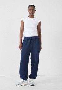 Camisa blanca de manga corta y pantalones de chándal azul marino oscuro. El conjunto presenta un ajuste relajado, una tela suave y una cintura con cordón. Combinado con zapatillas plateadas.