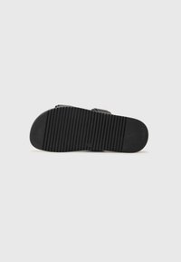 Svart sandalsole med en strukturerad, ribbad yta för grepp. Rundad framdel med en slät yta, utan synlig varumärkeslogotyp.