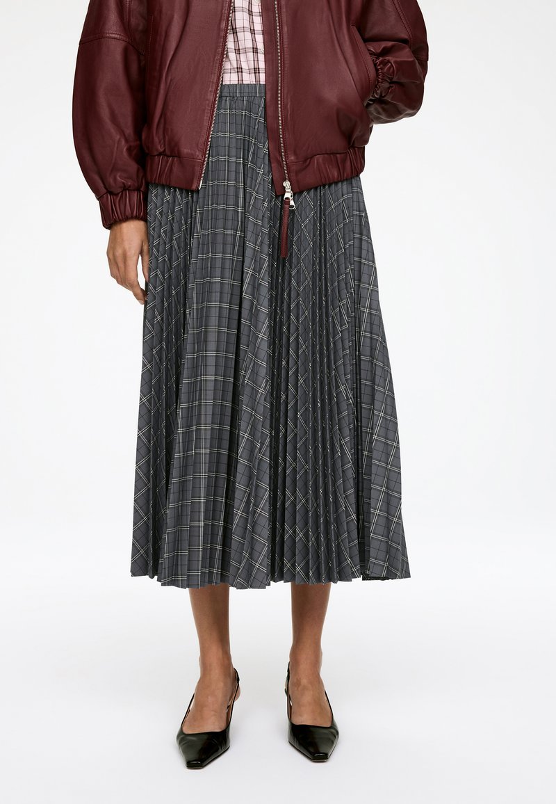 Jupe midi plissée grise avec un motif à carreaux, présentant des lignes verticales et horizontales. Assortie à une veste bomber en cuir bordeaux profond.