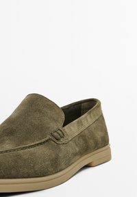 Chaussure slip-on en cuir suédé vert olive avec une texture lisse, une semelle en caoutchouc à profil bas et des coutures décoratives le long des coutures.