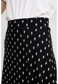 Falda negra con un patrón repetido de pequeños diamantes blancos. La tela parece suave con un ligero estiramiento, diseñada para una cintura ajustada.