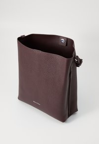 Sac fourre-tout en cuir bordeaux avec une surface texturée, un haut ouvert et une fermeture à pression. Présente un logo de marque visible à l'avant.