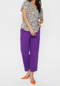 Top a maniche corte con motivo floreale in azzurro chiaro; abbinato a pantaloni morbidi viola e scarpe con punta arancioni.