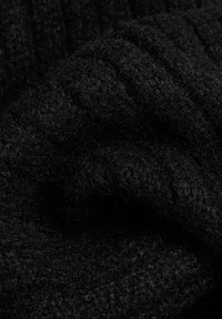 Schwarzer strukturierter Stoff, der einen dicken, weichen Strick mit ausgeprägten Rillen und einer fusseligen Oberfläche aufweist. Keine deutlichen Muster oder Akzente sichtbar.