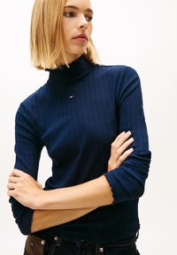 Μπλε ναυτικό ριμπ πουλόβερ με ζιβάγκο και μακριά μανίκια. Διαθέτει κυματιστό τελείωμα και διακριτική λεπτομέρεια λογότυπου στο στήθος. Λείο υλικό.