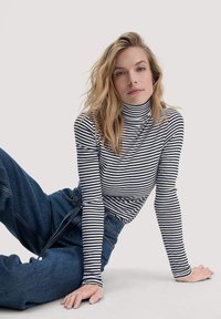 Langärmliges, Turtleneck-Oberteil mit schwarz-weißen, horizontalen Streifen, kombiniert mit locker sitzenden, dunkelblauen Jeans. Weicher Stoff, lässiges Design.