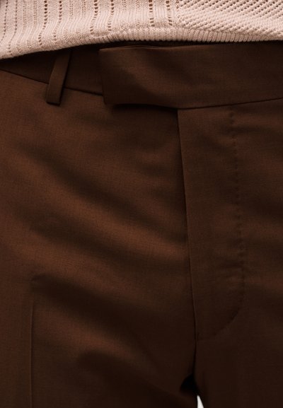 Κοντινό πλάνο καφέ ραμμένων παντελονιών με ταιριαστή θηλιά ζώνης και ορατό επάνω μέρος μπεζ πλεκτού πουλόβερ.