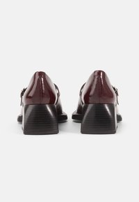 Burgundy patent leather shoes with square toes and a low block heel, featuring metal accents and a smooth, glossy finish.