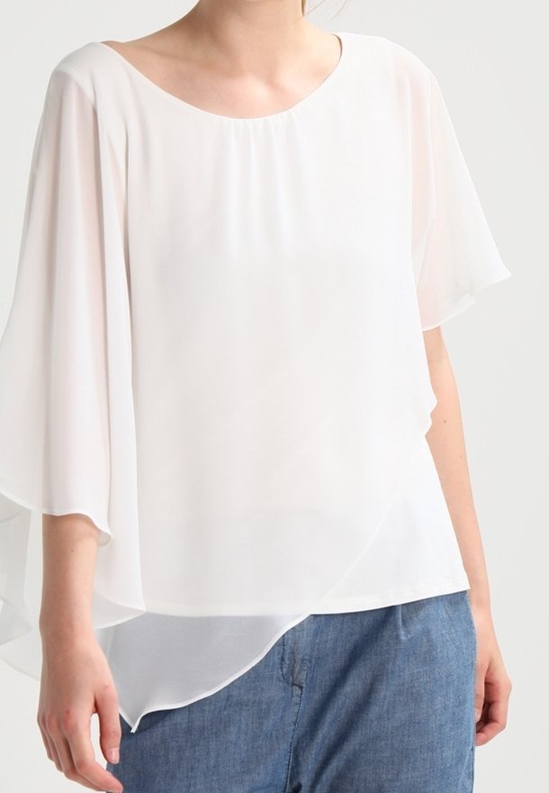 Blouse blanche et légère avec un col rond et des manches fluides et transparentes. L'ourlet asymétrique apporte un intérêt visuel. Texture lisse.