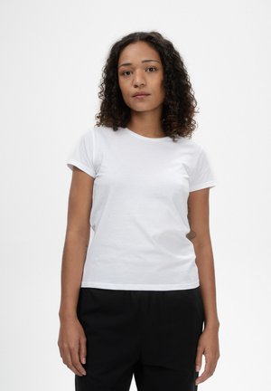 Weißes Baumwoll-T-shirt mit Rundhalsausschnitt und kurzen Ärmeln, getragen mit schwarzen Hosen, die ein schlichtes Design und eine weiche Textur aufweisen.