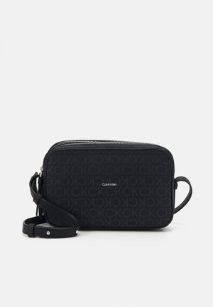Zwarte rechthoekige Calvin Klein crossbodytas met herhalend CK-patroon en verstelbare riem op witte achtergrond.