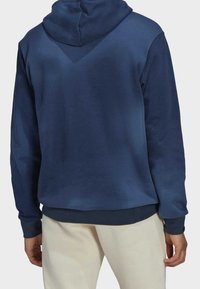 Námořnická modrá mikina s kapucí vyrobená z měkké tkaniny, obsahující klokánkovou kapsu a žebrované manžety. Hladká textura se uvolněným střihem.