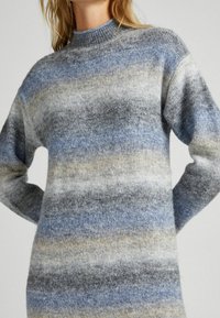 Maglione lavorato a maglia in un motivo ombre blu, grigio e beige. Texture morbida con un collo alto e maniche lunghe. Vestibilità rilassata e cuciture minime.