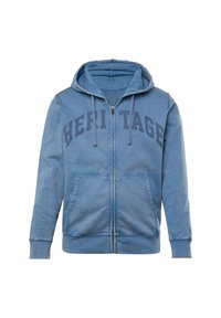Zip-up hoodie in faded blue, featuring a front kangaroo pocket, drawstring hood, and bold "HERITAGE" print across the chest.