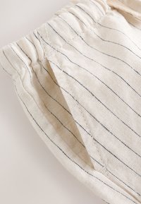 Close-up of beige fabric with thin vertical black stripes and gathered elastic waistband, showing a front pocket detail.