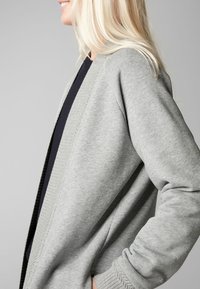 Cardigan grigio realizzato in tessuto morbido, con una vestibilità comoda, apertura frontale e rivestimento interno scuro a contrasto. Dettagli a coste sui polsini e sull'orlo.