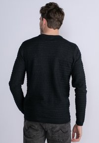 Pull nero in tessuto a maglia con maniche lunghe e colletto a girocollo, caratterizzato da un sottile motivo a righe e polsini a coste.