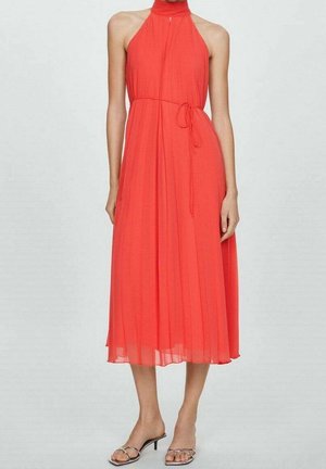 Robe corail à col licou, longueur mi-mollet, tissu plissé, corsage ajusté avec détail noué, texture lisse, associée à des chaussures argentées à brides.