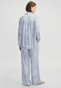 Conjunto de loungewear de tejido texturizado en azul claro que incluye una camiseta de manga larga con un pliegue en la parte trasera y pantalones de pierna ancha. Diseño minimalista.